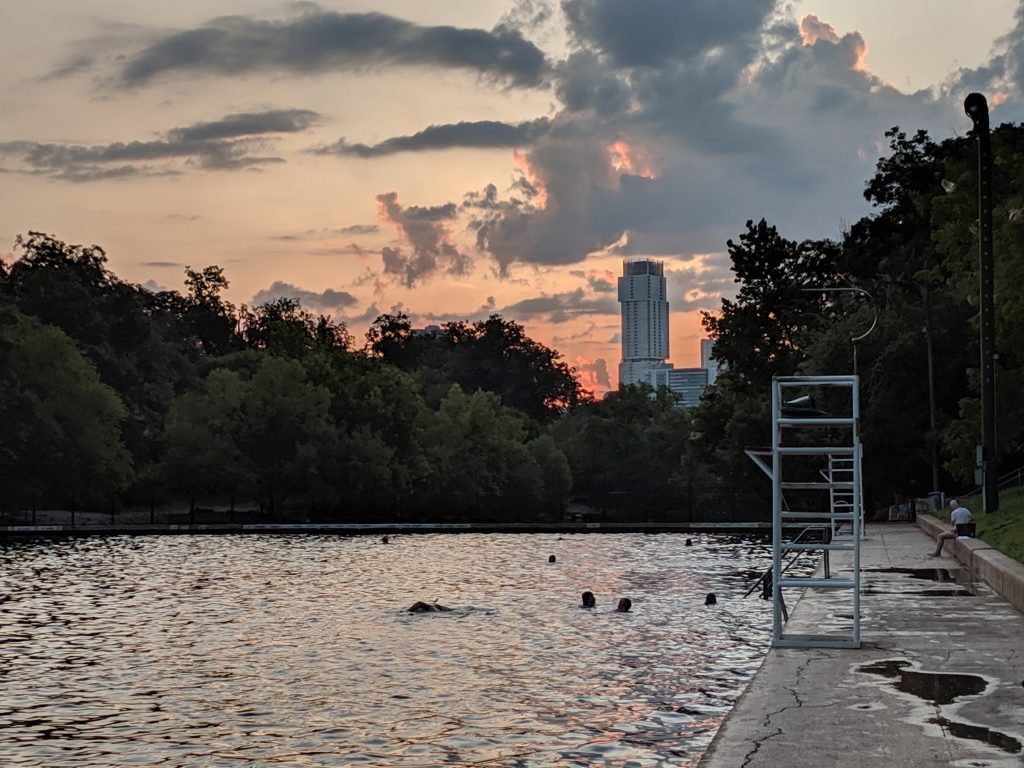 Swimmers enjoying Barton Springs Pool during a picturesque sunset.