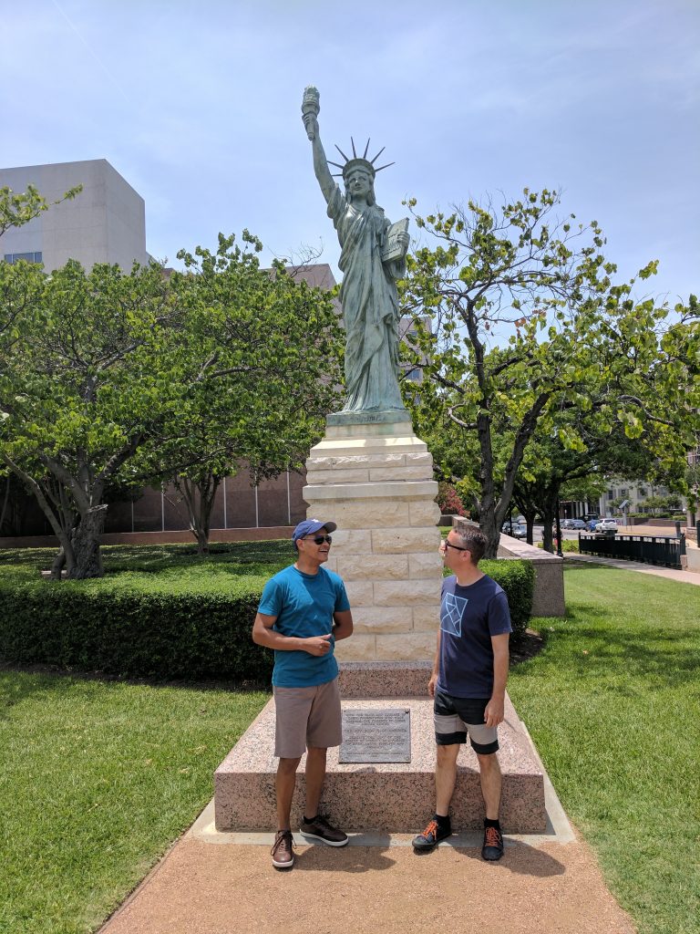 Unique Austin: Two people stand in front of a small statue of liberty on the capitol grounds.