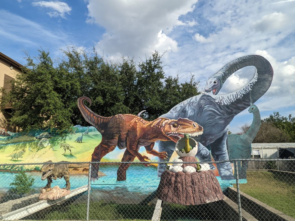 Exterior of the Jurassic Car Wash in Austin, featuring a metal fence with 2D dinosaur sculptures behind it.