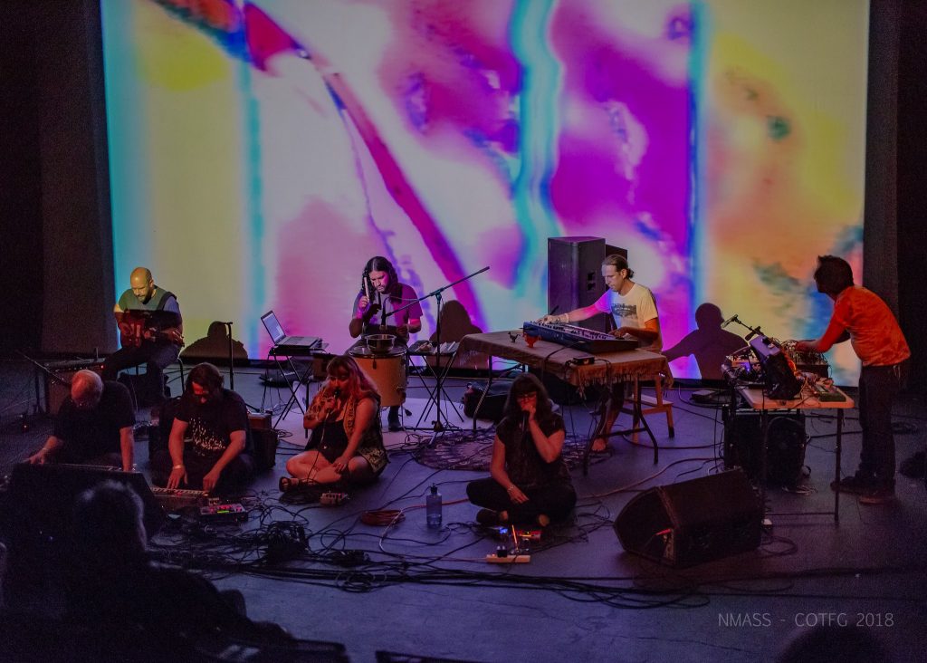 Musicians playing in front of a projection screen playing colored shapes.