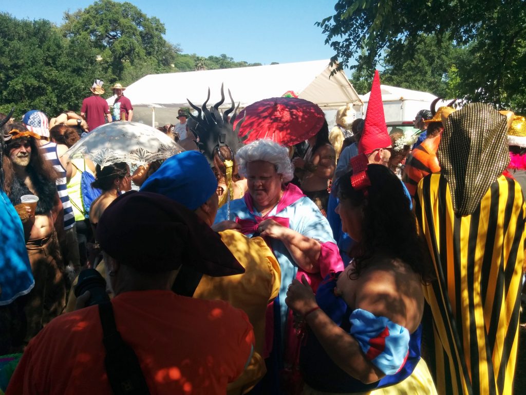 Outdoor scene at Eeyore's Birthday event in Austin, featuring costumed people talking in a crowded area.