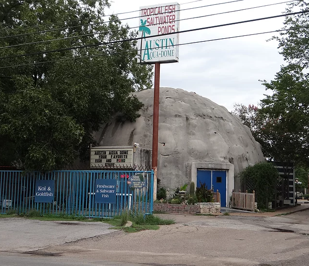 Exterior of the Austin-Aqua Dome, a round building with a fake rock surface, located on a street corner.