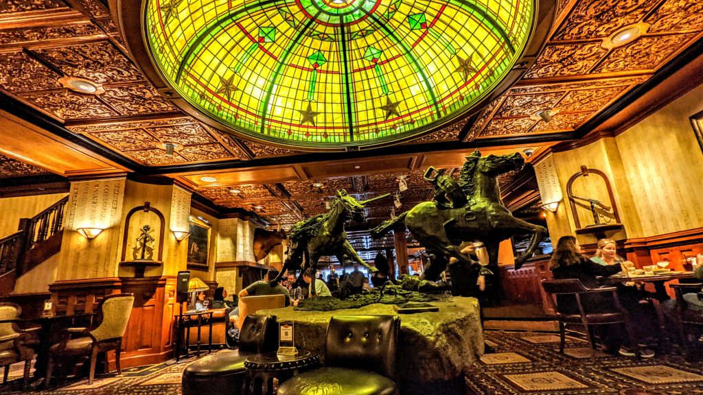 The Driskill Bar, Austin, Texas. Horse statue under a green lit dome in a western themed bar. Guns.