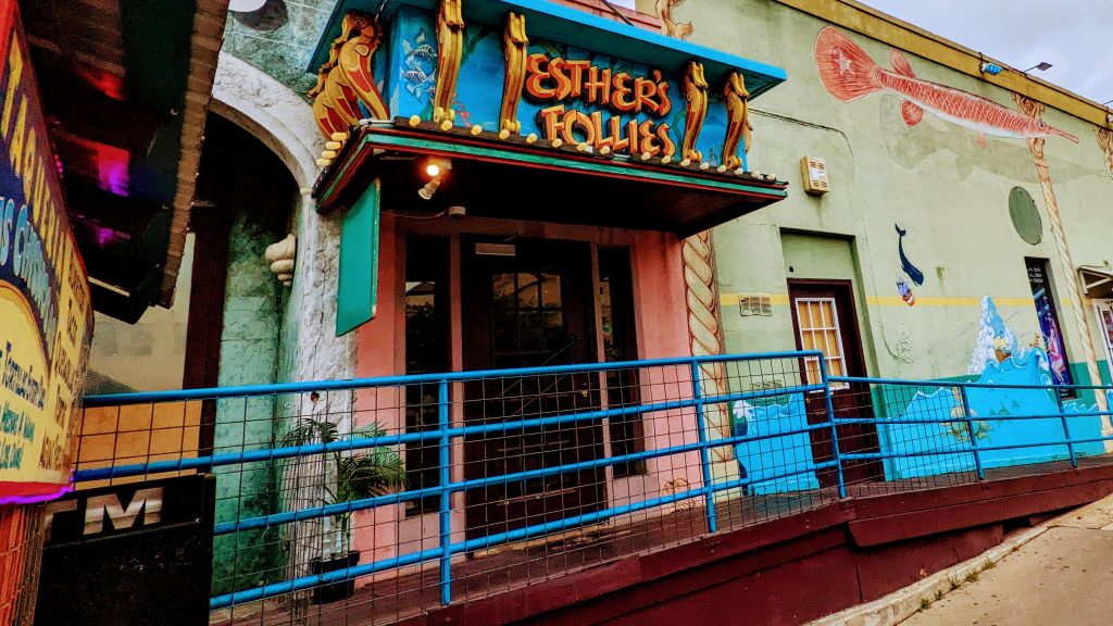 Entrance of Esther's Follies in Austin, Texas, featuring a mural facade and a blue railing.