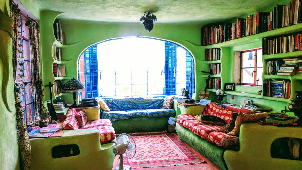 A vintage-styled living room inside the Casa Neverlandia with green walls, three couches and a red patterned rug.